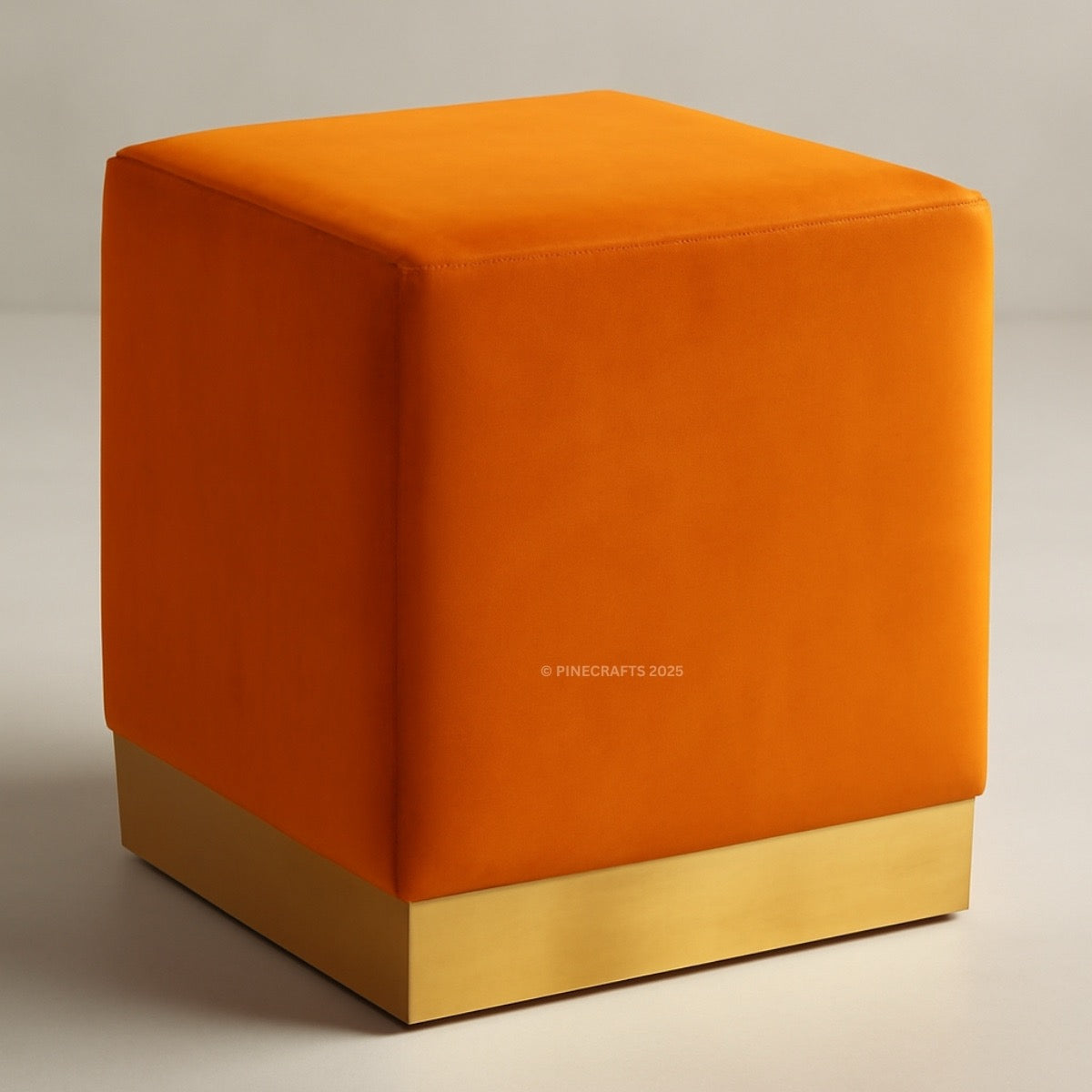 Orange cube-shaped ottoman with a gold base on a neutral background