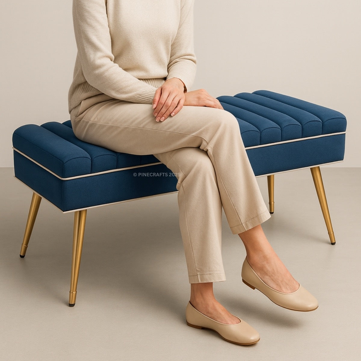 Person sitting on a blue ottoman with gold legs against a neutral background