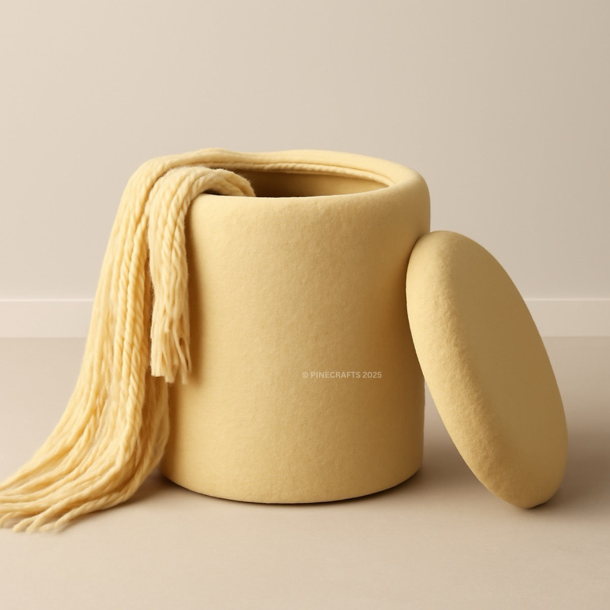 Beige storage bin with a matching lid and a beige blanket draped over it on a beige background.