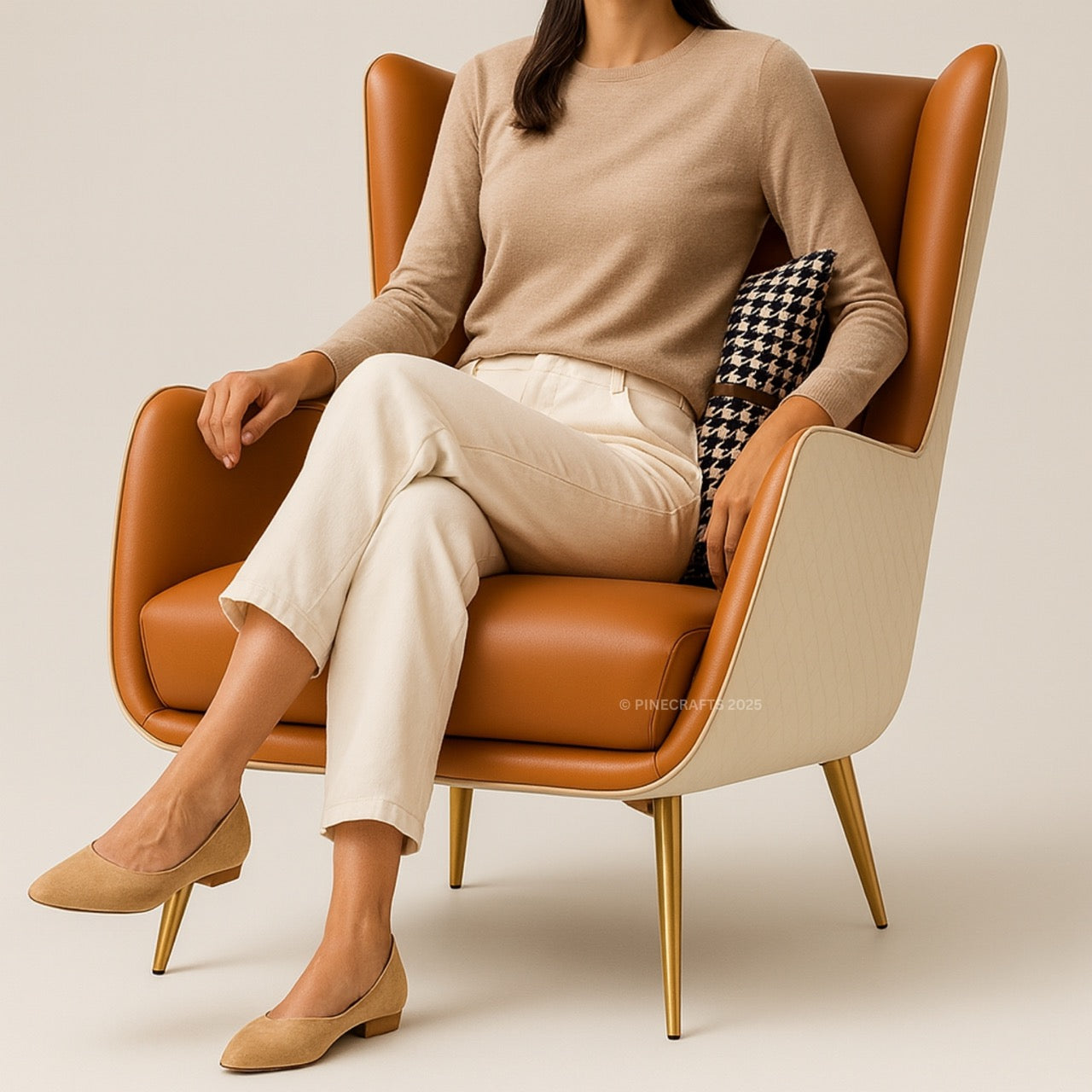 Woman sitting on a brown chair wearing a beige sweater and pants, with a neutral background.