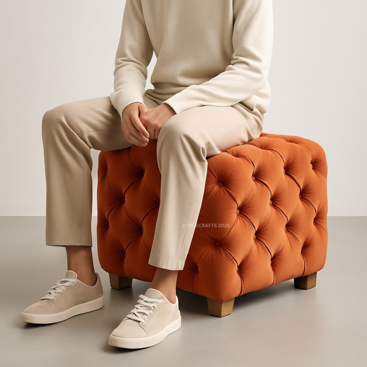 Person sitting on an orange tufted ottoman with beige pants and white shoes.