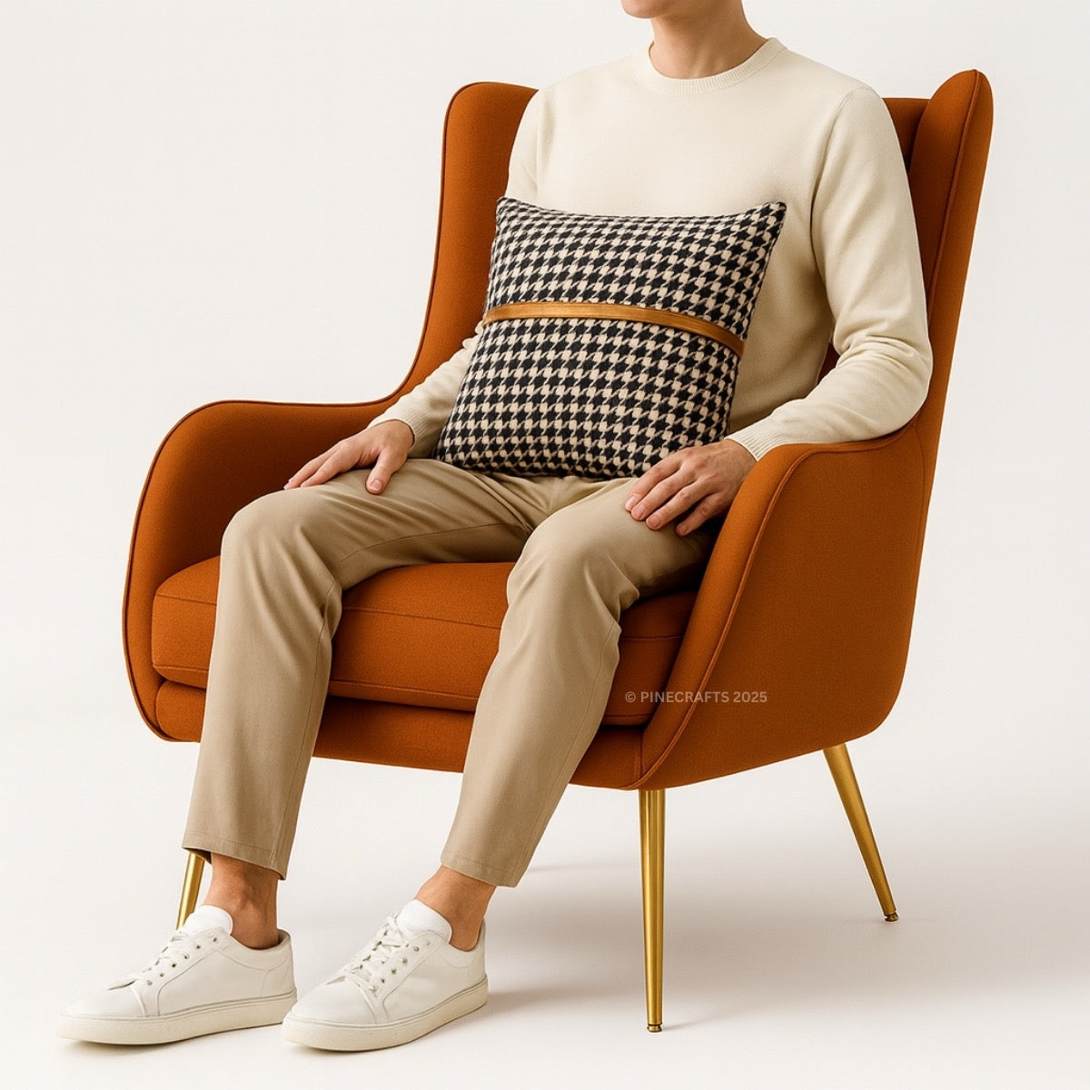 Person sitting on an orange armchair with a houndstooth patterned pillow, wearing a beige sweater and pants with white sneakers.