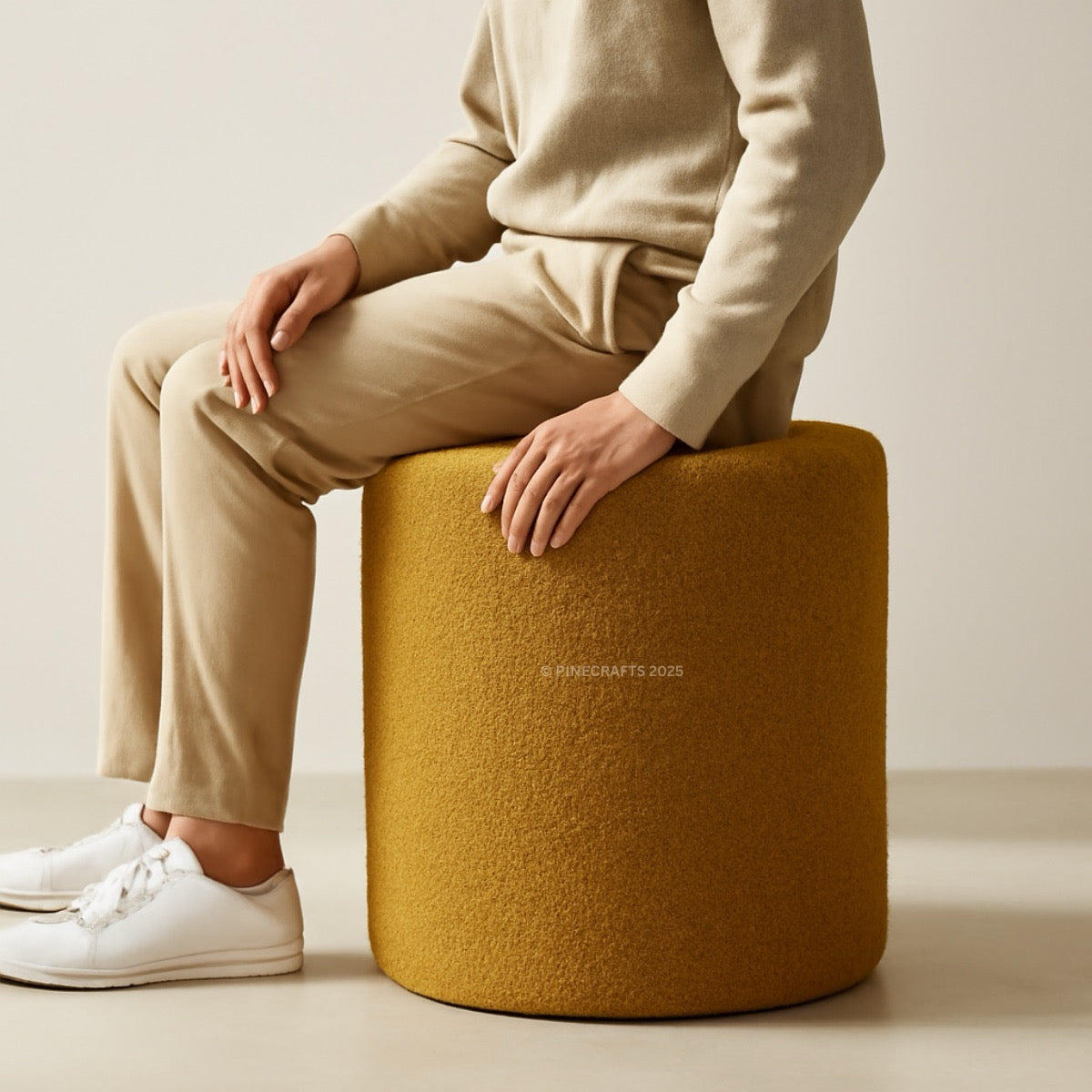 Person sitting on a mustard yellow pouf with a neutral background