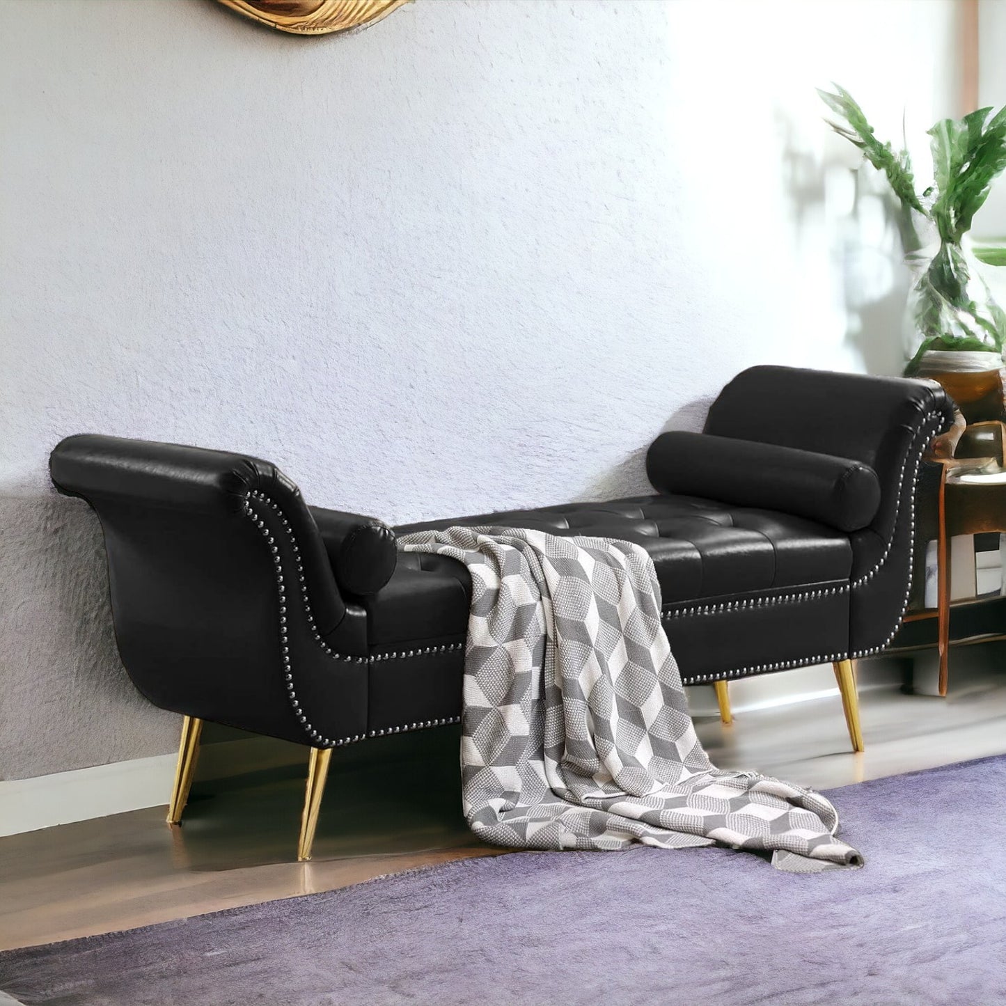 A black velvet button tufted 3-seater sofa with gold legs, placed in a living room setting with a grey throw blanket and a decorative plant in the background.