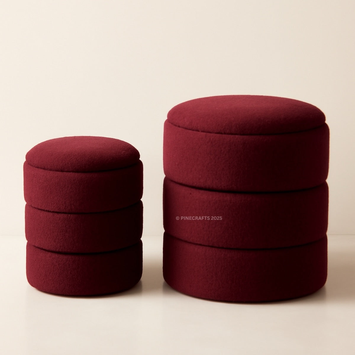 Two maroon fabric ottomans stacked on a beige background