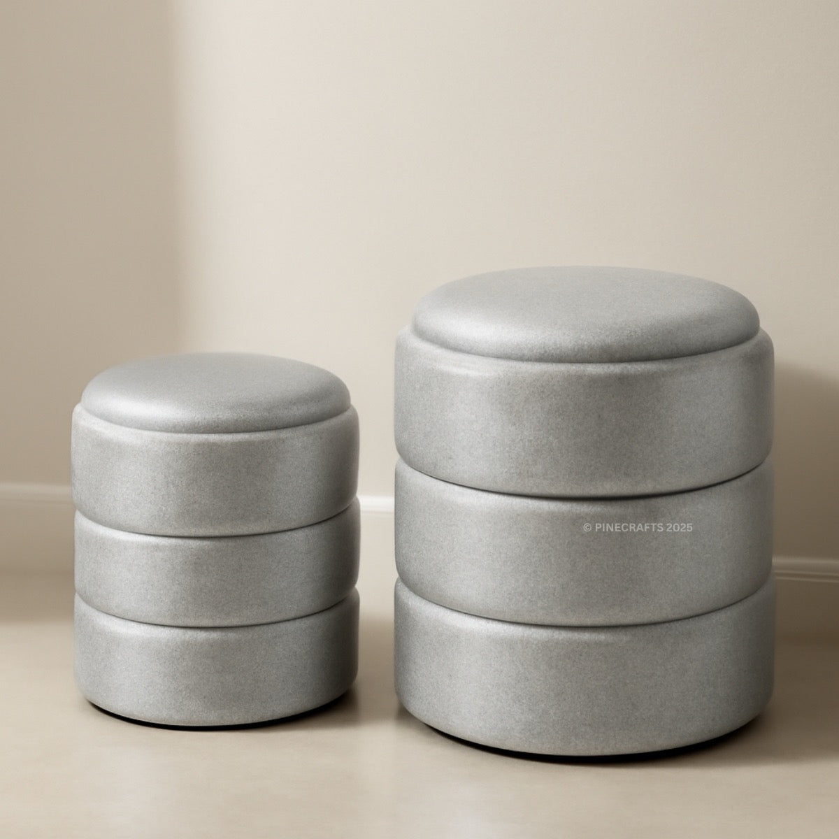 Two gray ottomans stacked on top of each other against a beige wall.