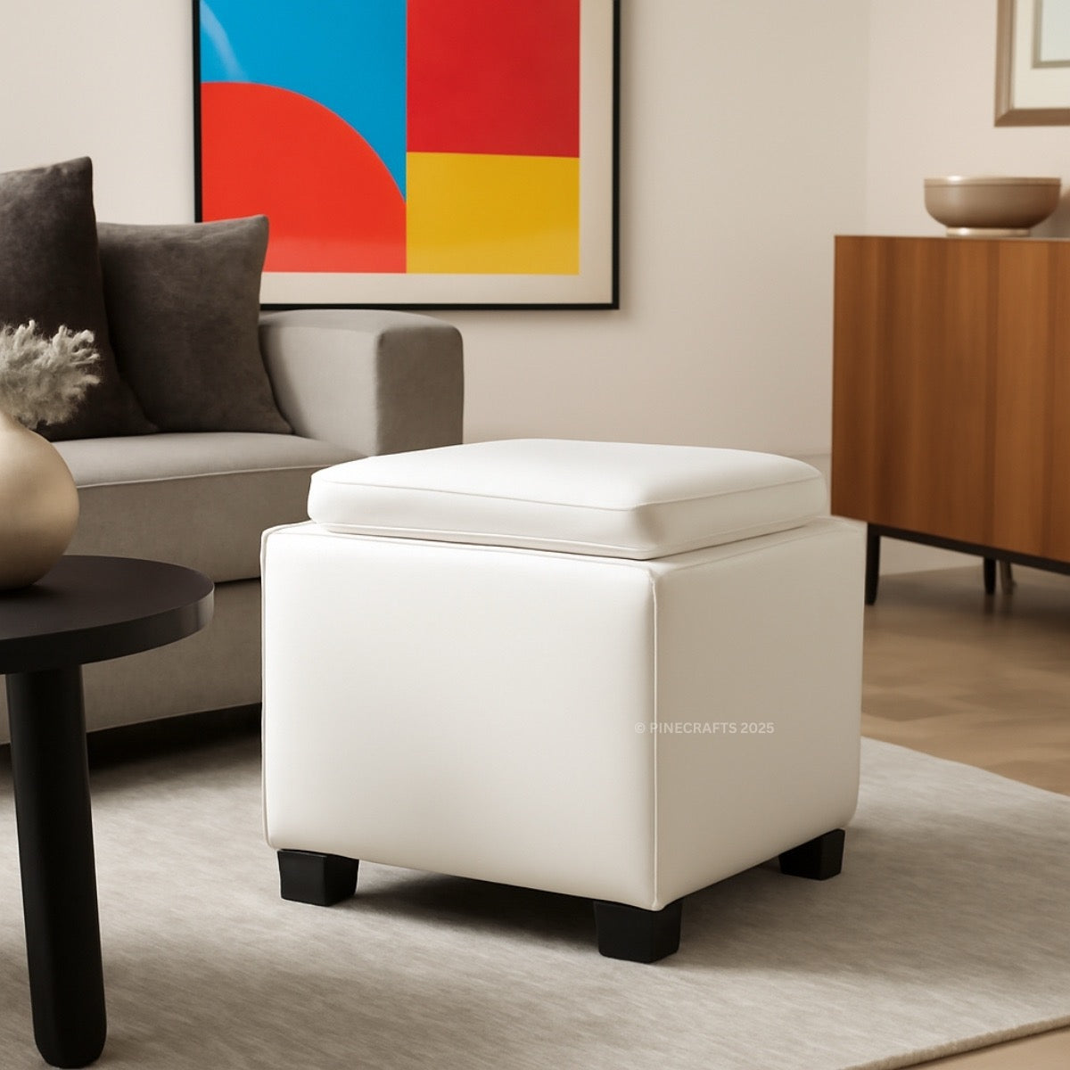 White storage ottoman in a living room setting with a colorful abstract painting on the wall.