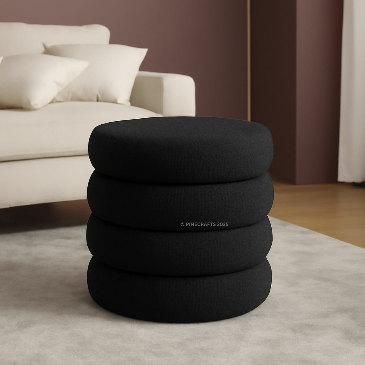 Stack of black cushions on a light gray rug with a beige sofa in the background
