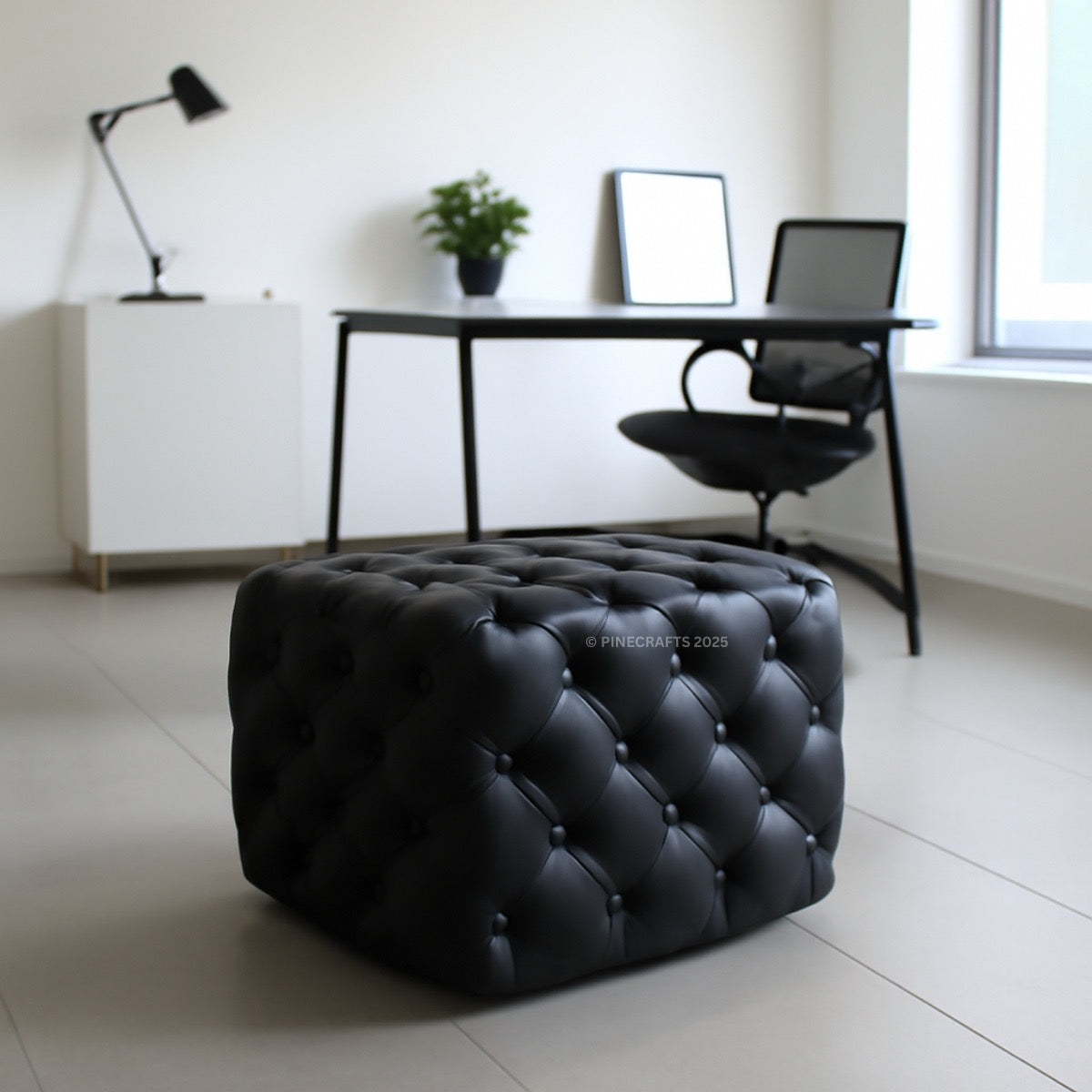 Black tufted ottoman in a modern room with a desk and lamp.