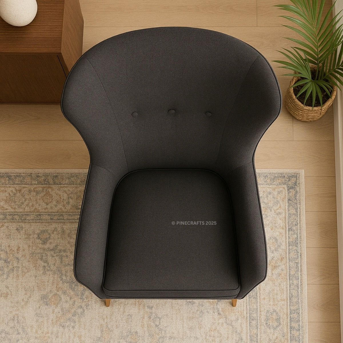 Black armchair on a wooden floor with a plant and side table in the background