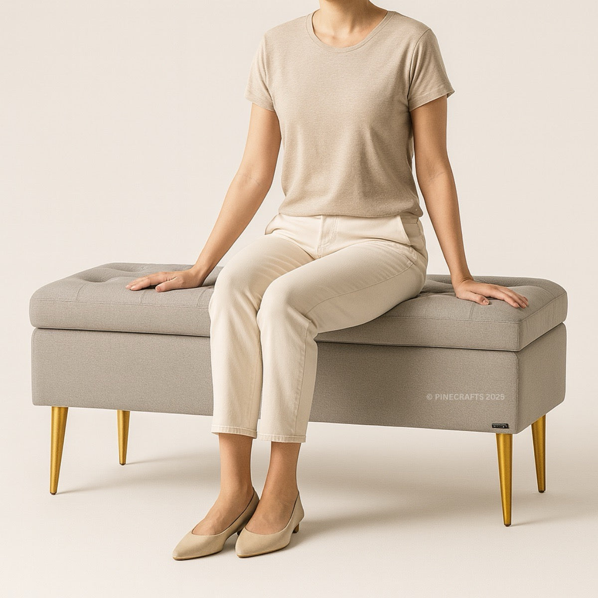 Person sitting on a gray upholstered bench with gold legs against a beige background