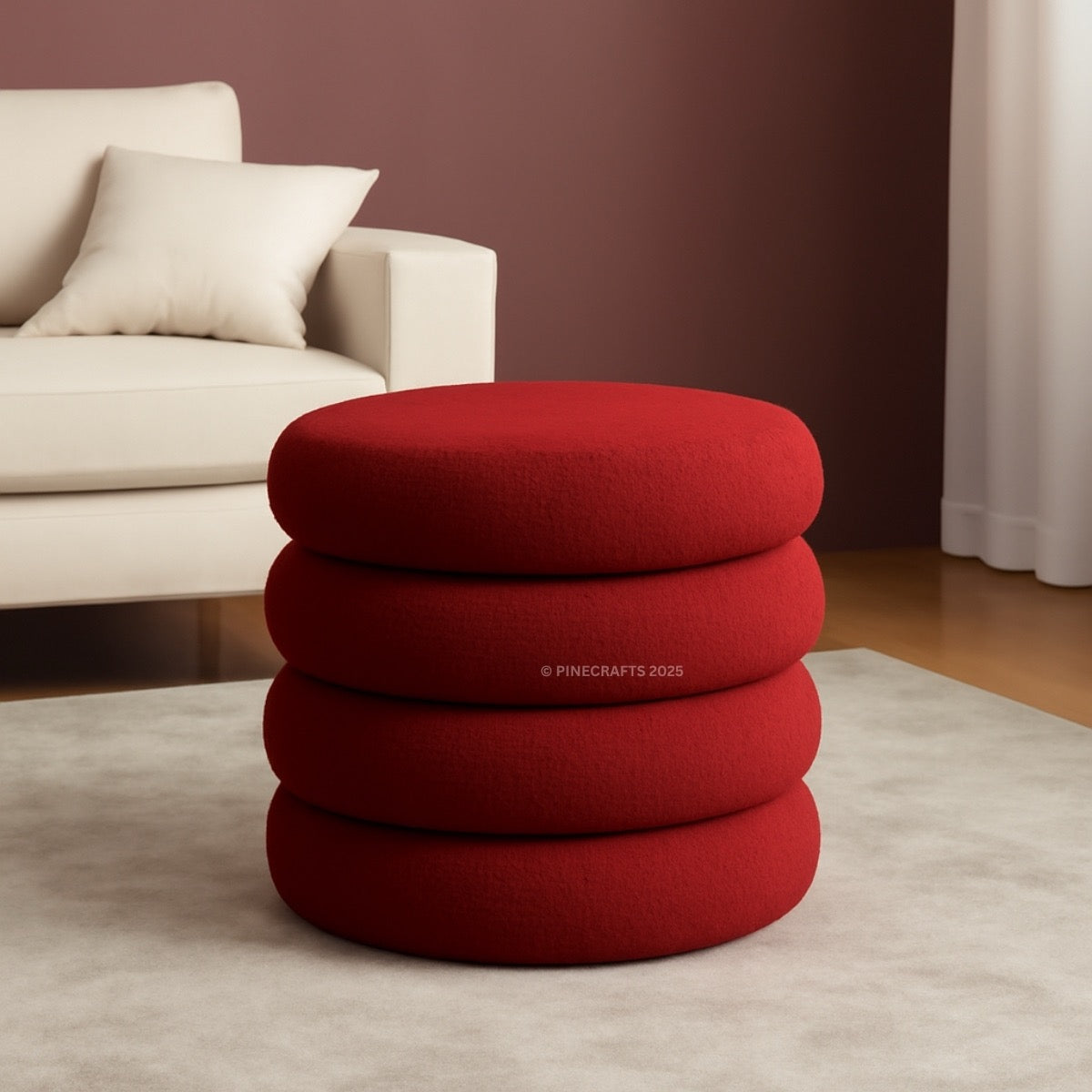 Stack of red cushions on a light gray rug with a beige sofa and dark brown wall in the background.