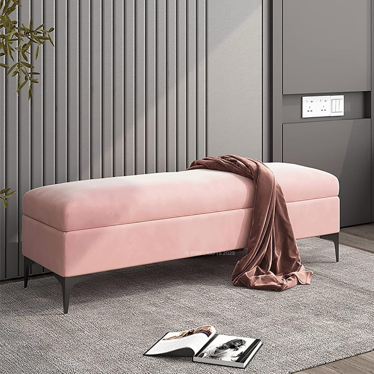 Pink ottoman with a brown blanket in a room with gray walls and a plant.