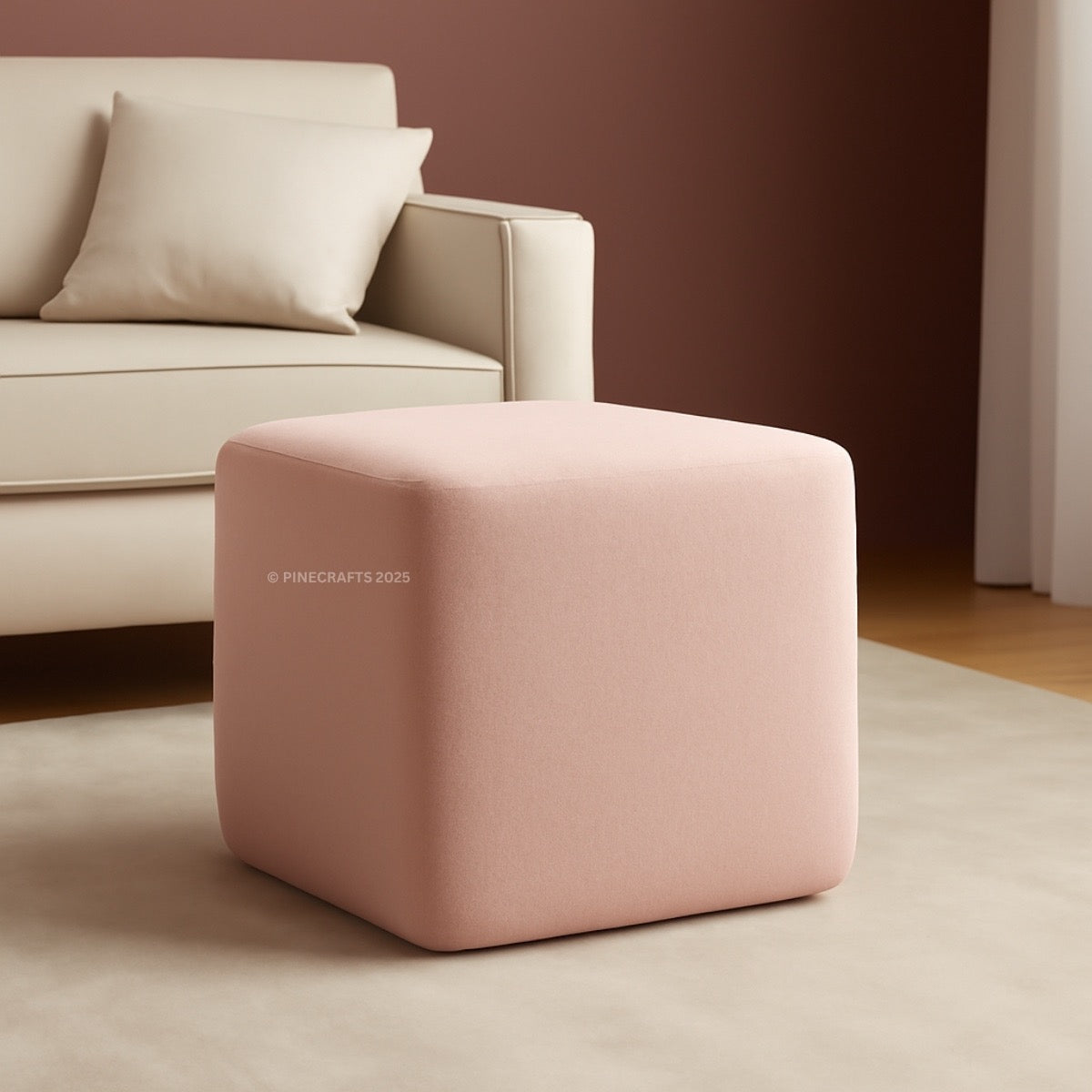 Pink cube-shaped ottoman in front of a beige sofa against a brown wall.