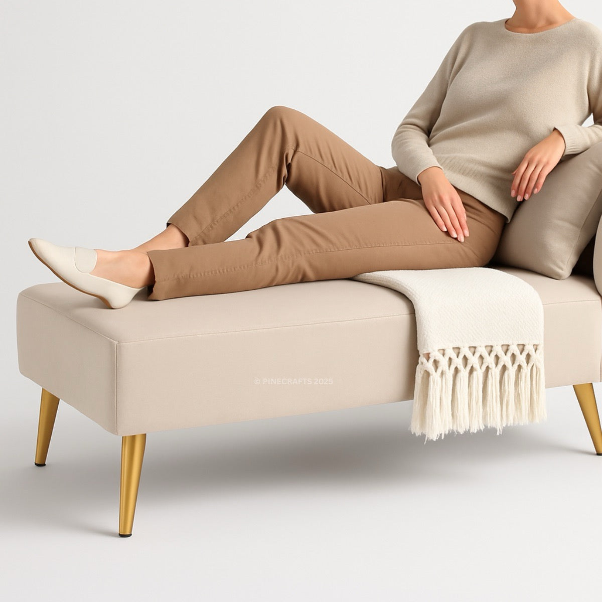 Person sitting on a beige bench with gold legs, wearing brown pants and a beige sweater.