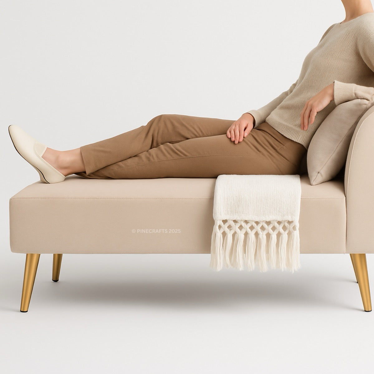 Person sitting on a beige bench with gold legs, wearing brown pants and a beige sweater.