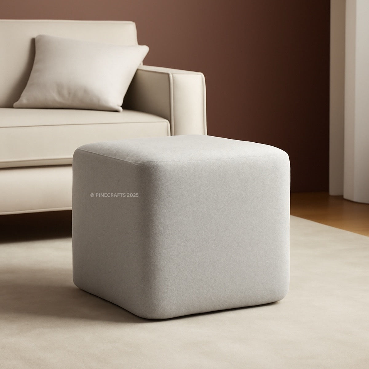 Gray cube-shaped ottoman in front of a beige sofa with a brown wall background.