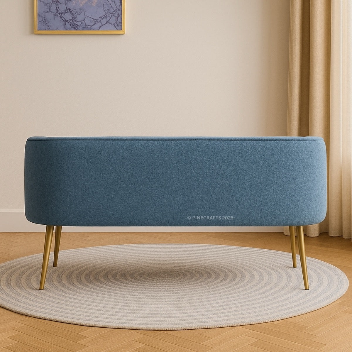 Blue upholstered bench with gold legs on a wooden floor in a room with beige walls and a round rug.