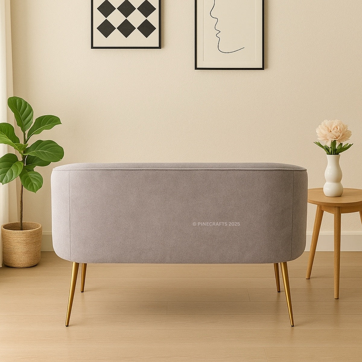 Gray ottoman with gold legs in a room with a plant and small table.