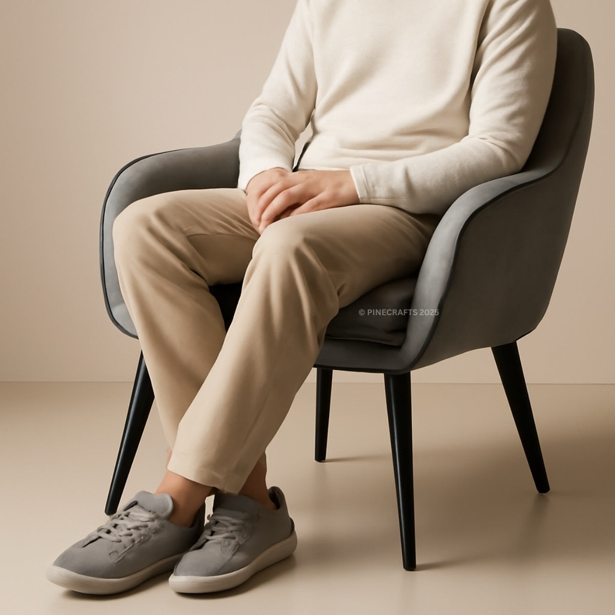 Person sitting on a chair wearing beige pants and gray sneakers against a beige background