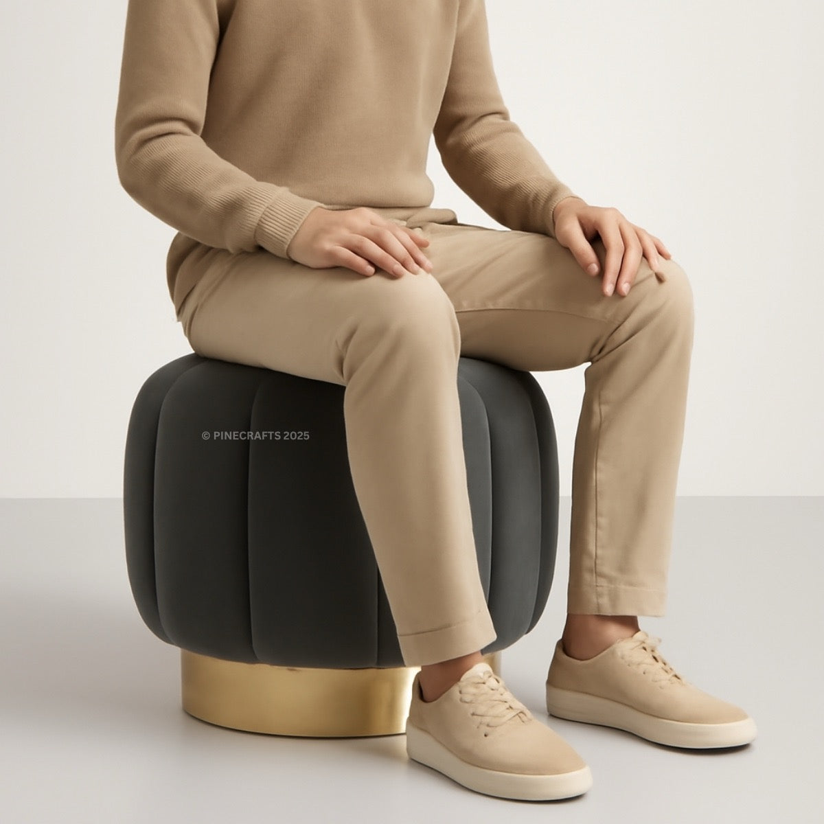 Person sitting on a modern black and gold stool wearing beige pants and shoes.