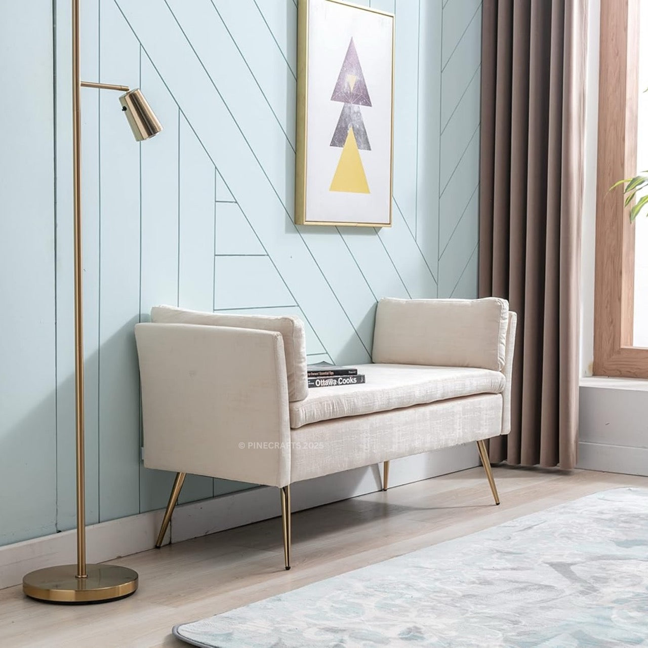 Beige sofa with gold legs in a room with a light blue wall, framed art, and a standing lamp.