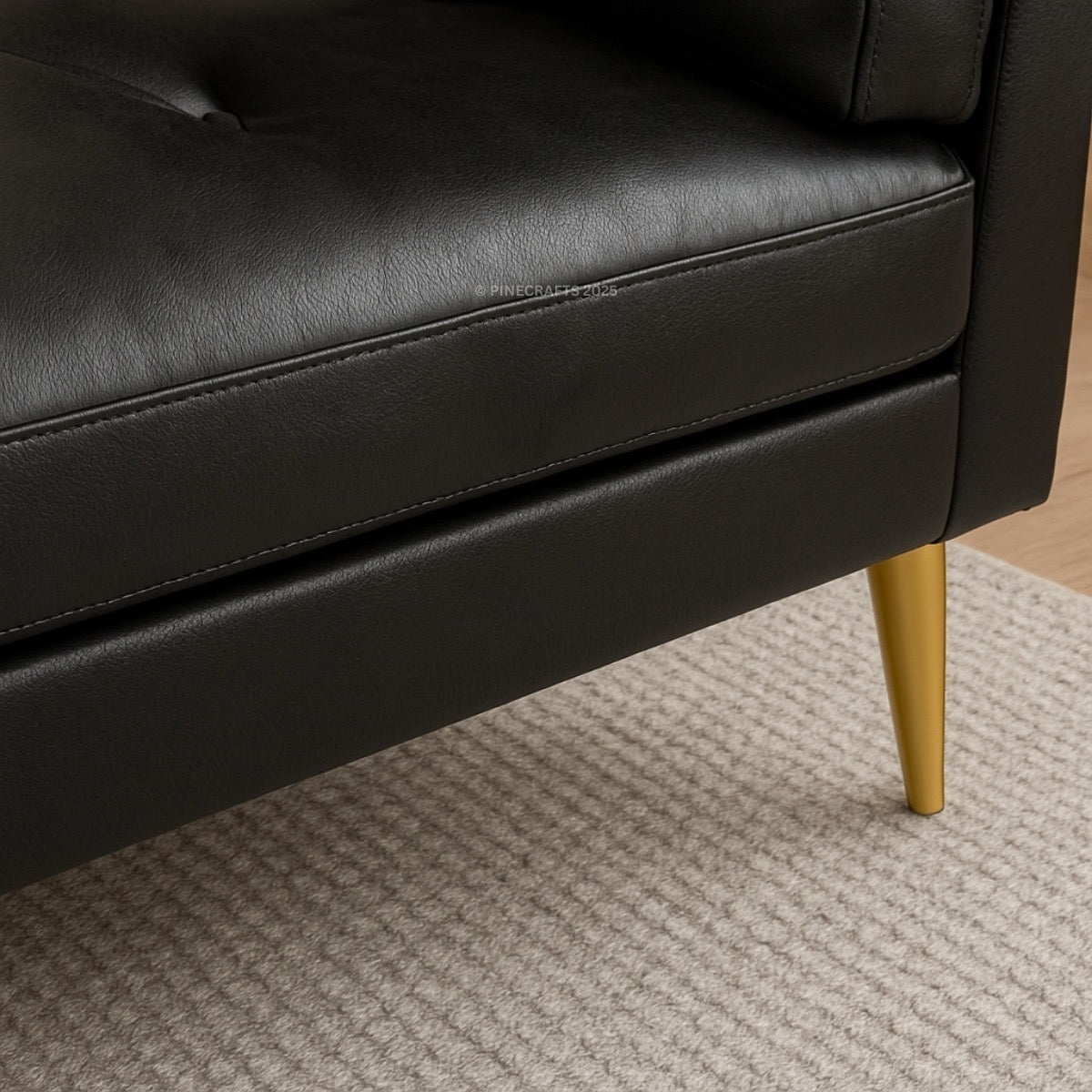 Close-up of a black leather sofa with gold legs on a carpeted floor.