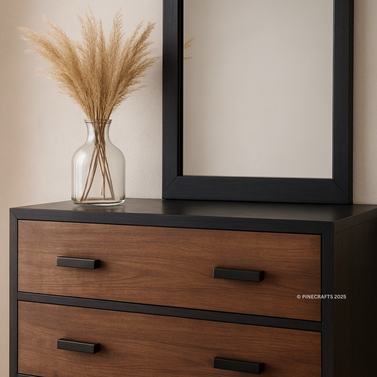 Wooden dresser with black accents, mirror, and vase with dried plants on a beige wall.