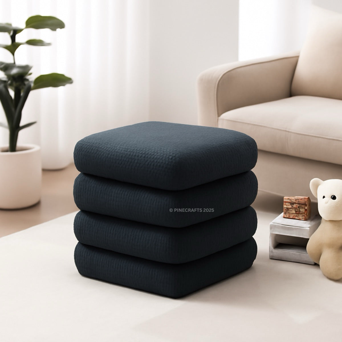 Stack of dark blue cushions on a light-colored floor with a beige sofa and plant in the background.