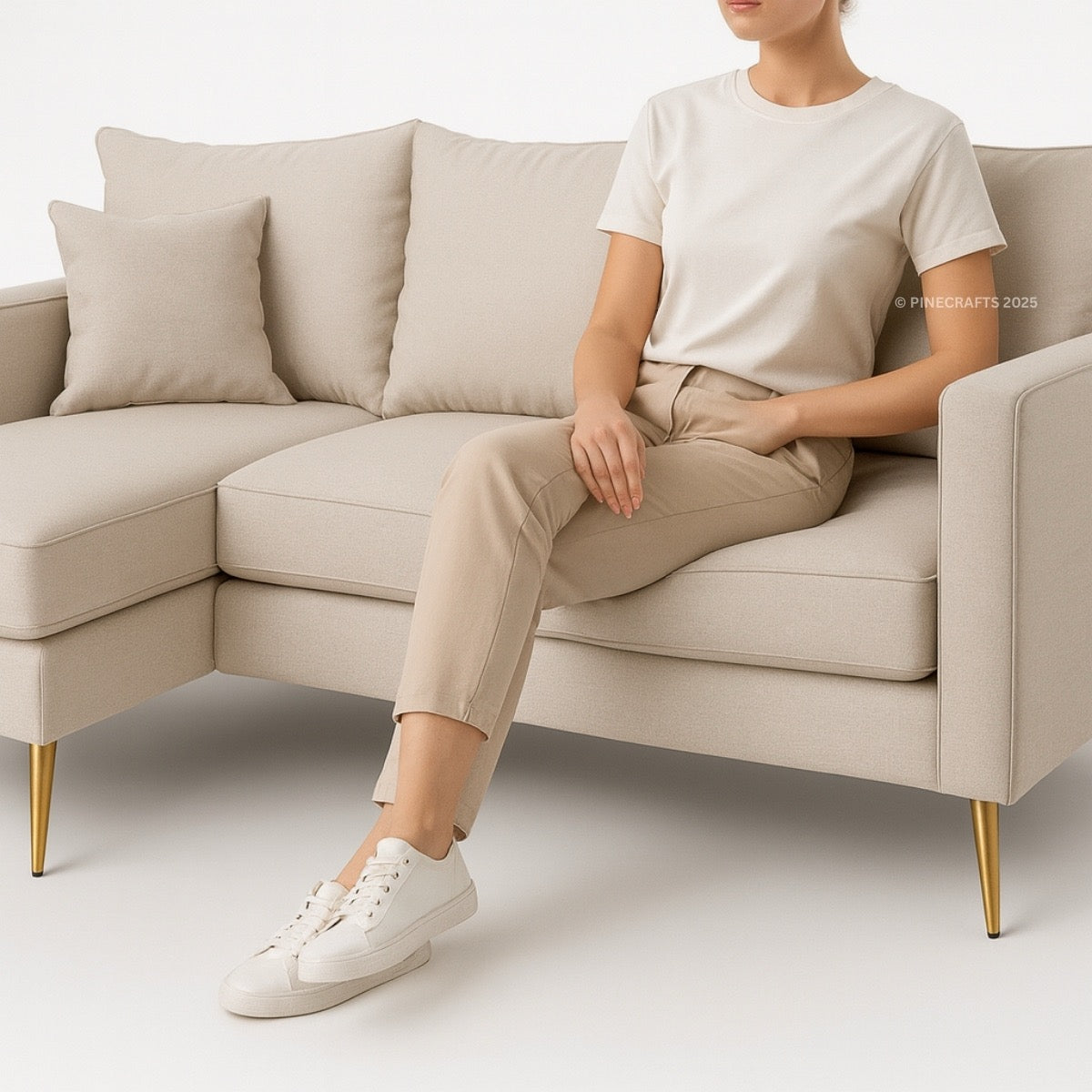 Person sitting on a beige sectional sofa wearing a white t-shirt, beige pants, and white sneakers.