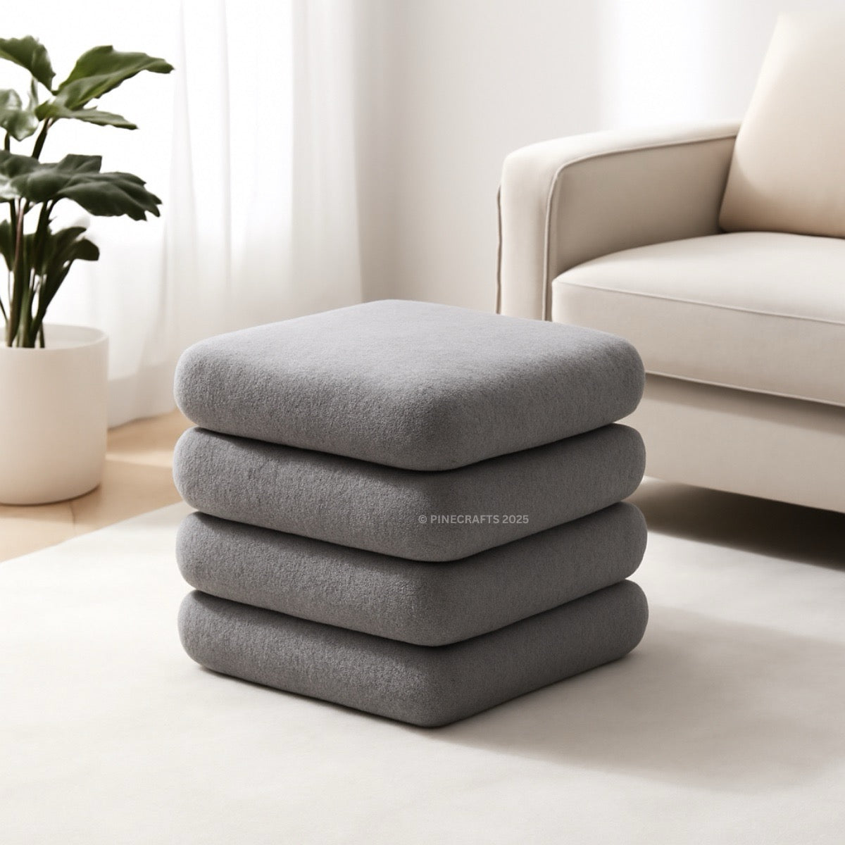 Stack of gray cushions on a light-colored floor with a beige sofa and plant in the background.