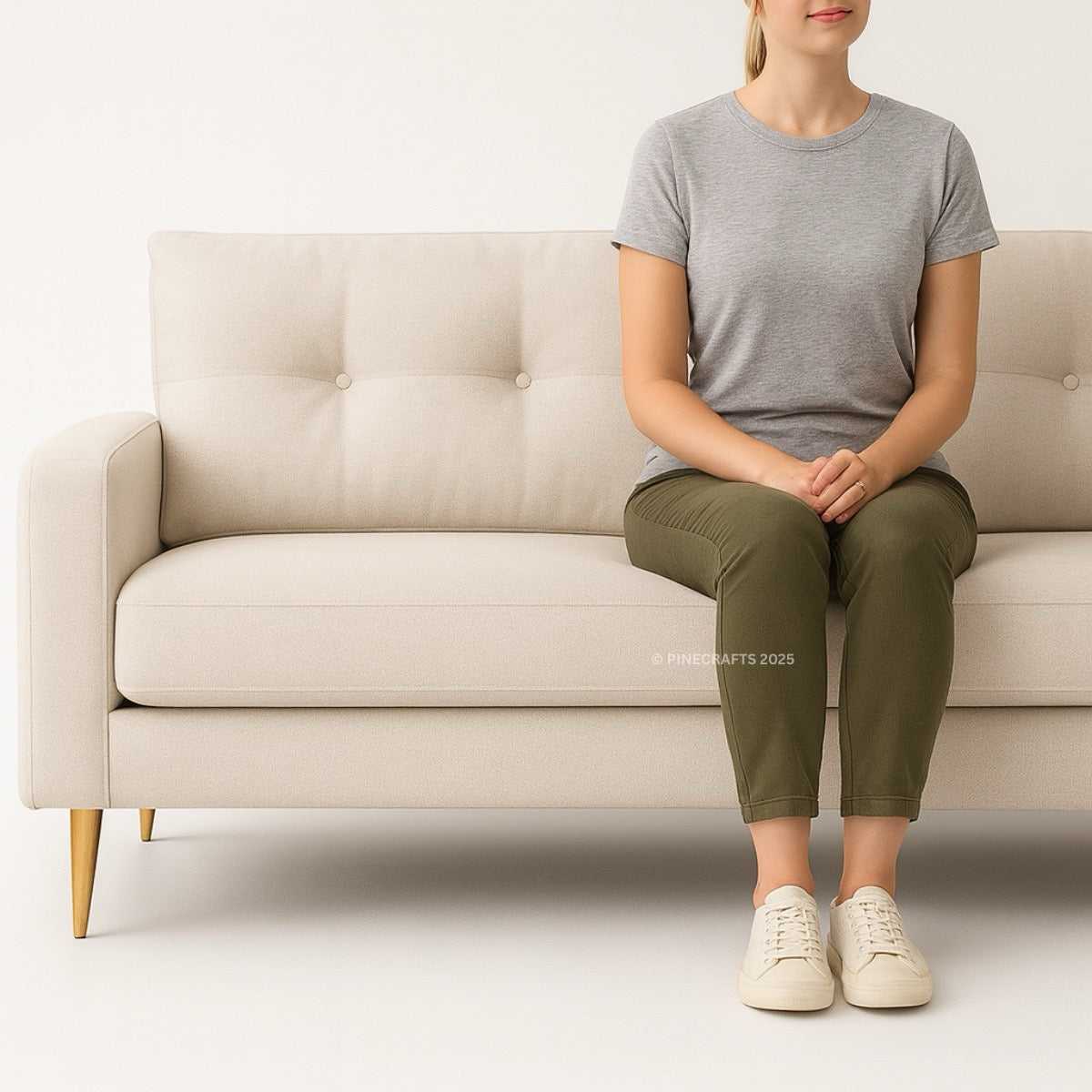 Person sitting on a beige sofa wearing a gray t-shirt, green pants, and white sneakers.