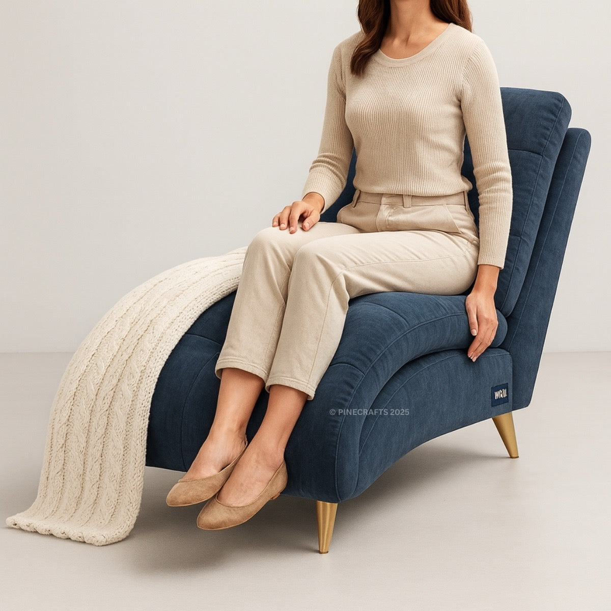 Woman sitting on a blue armchair with a beige blanket, wearing a beige outfit.