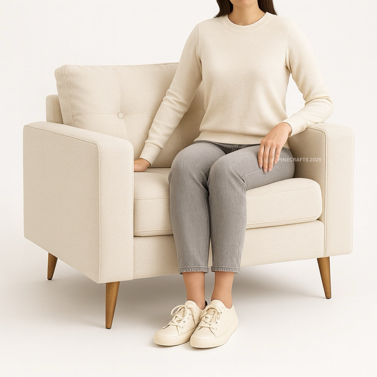 Person sitting on a beige armchair wearing a beige sweater, gray pants, and white sneakers.