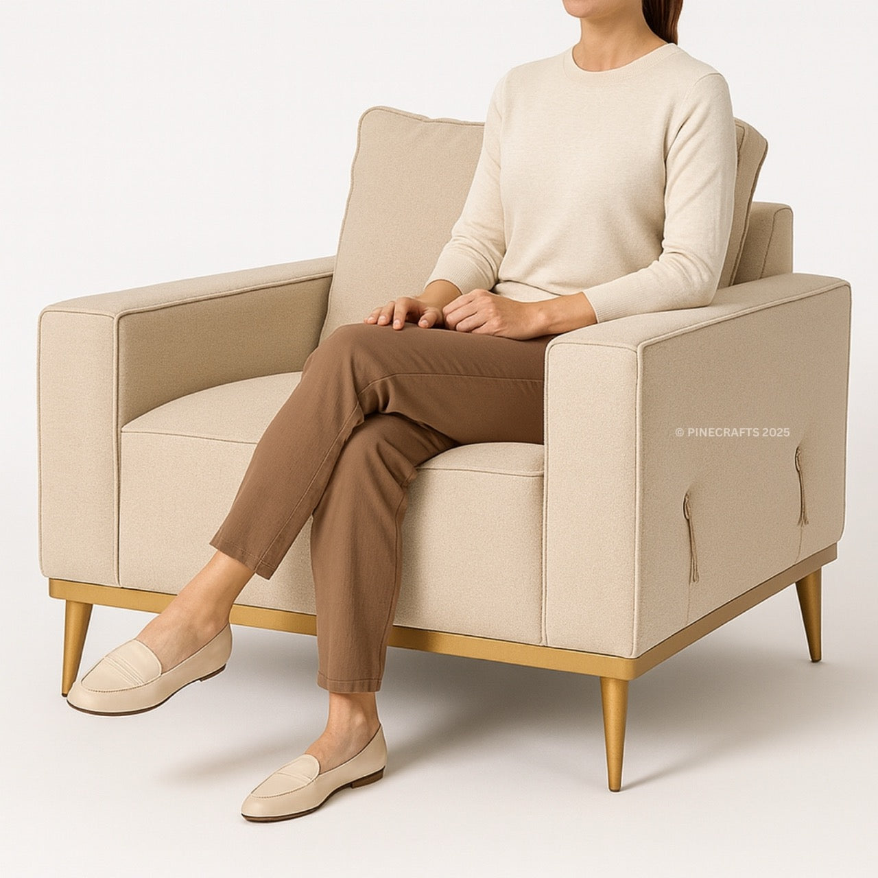 Person sitting on a beige armchair wearing a cream sweater and brown pants.