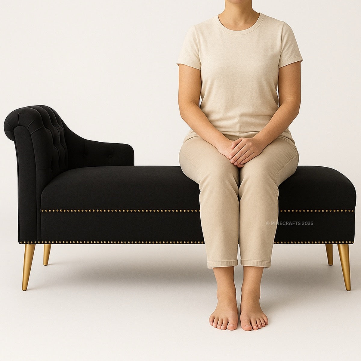 Person sitting on a black bench wearing beige clothing against a white background