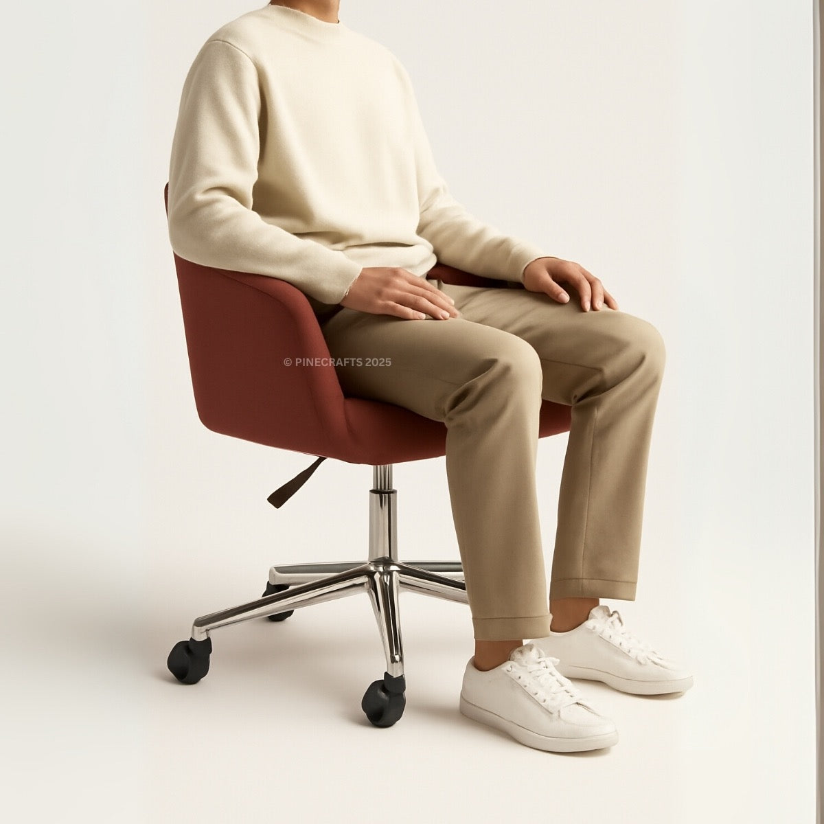 Person sitting on a red office chair wearing a beige sweater, beige pants, and white sneakers.