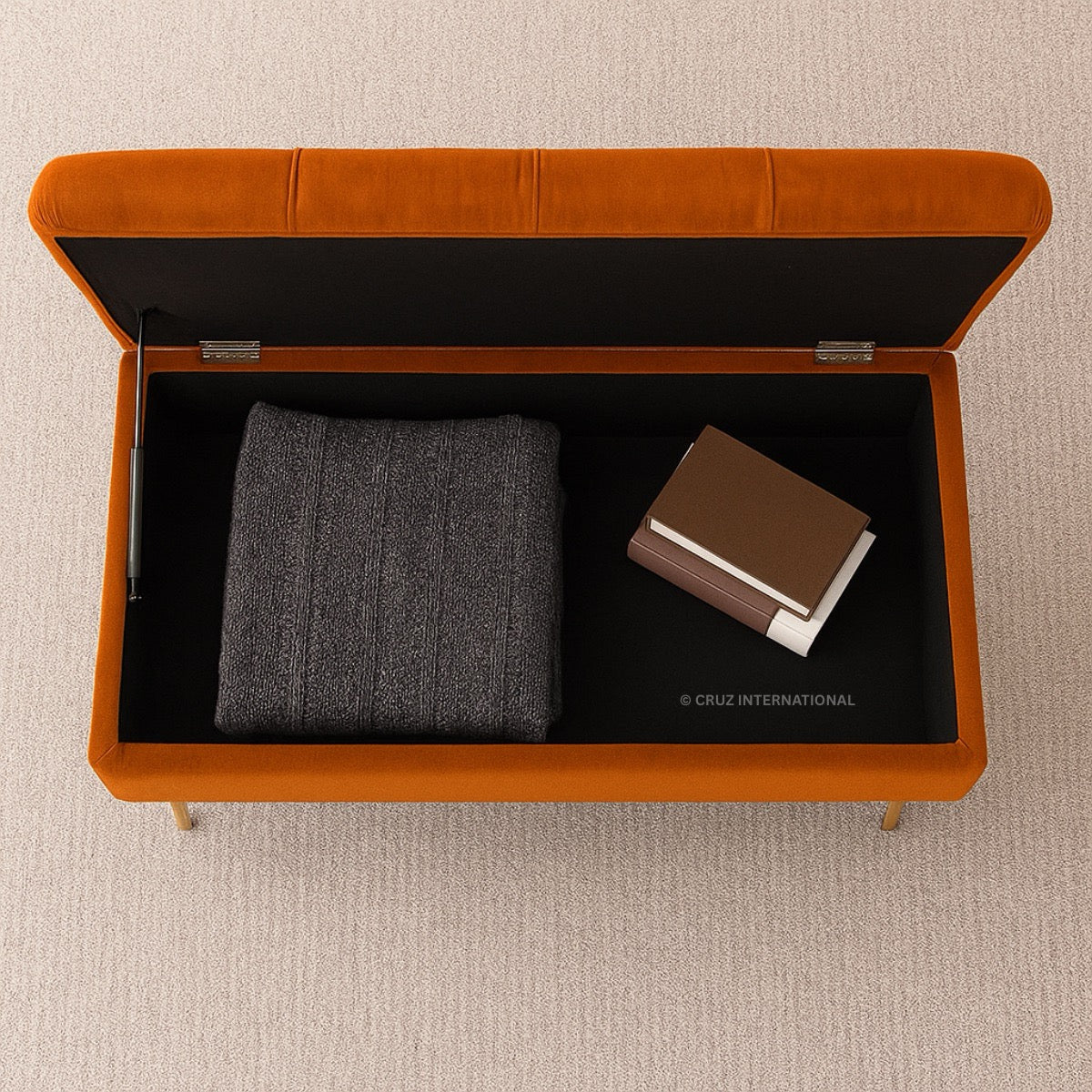 Orange storage bench with a black interior containing gray fabric and a brown book on a beige carpet.
