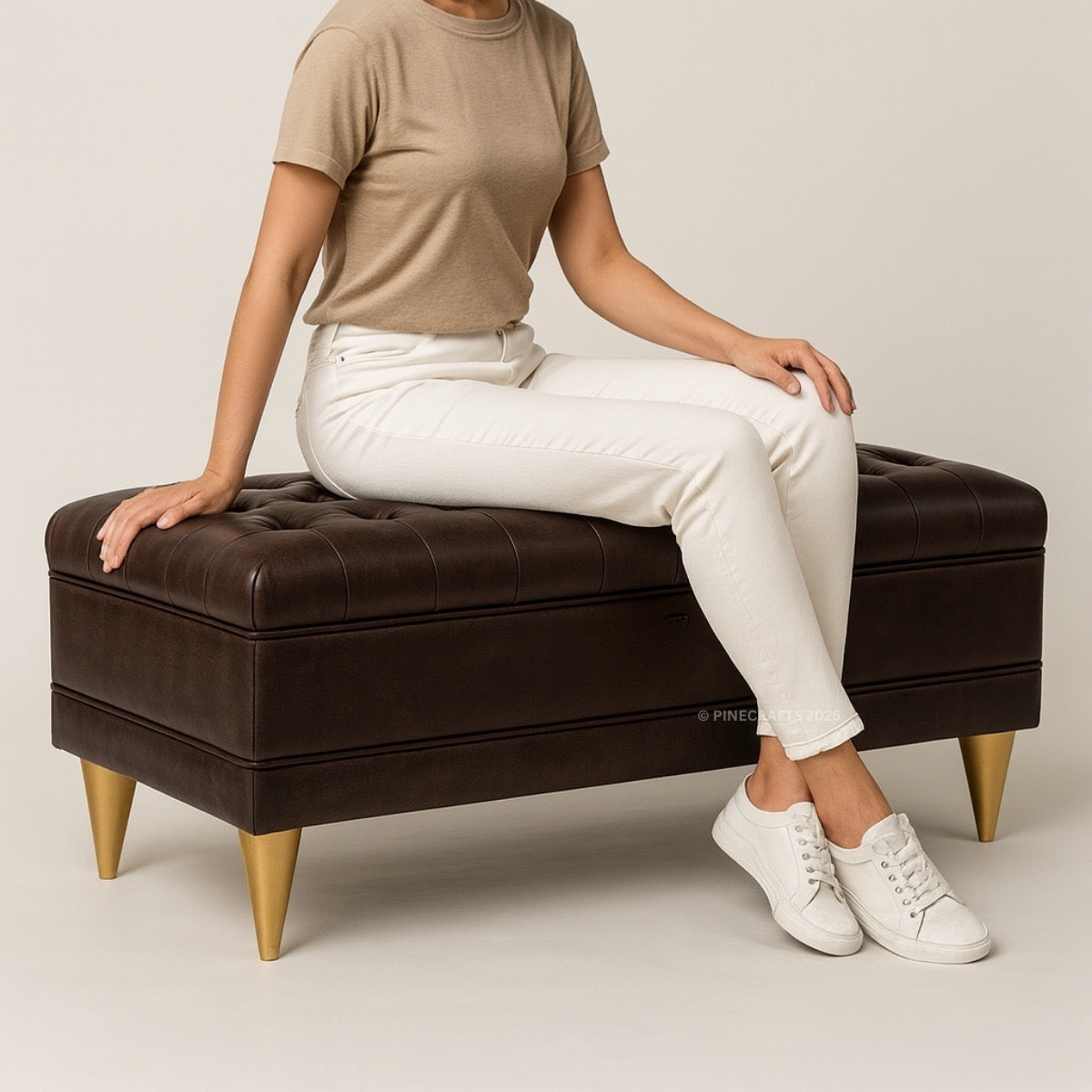 Person sitting on a brown leather ottoman with gold legs against a plain background