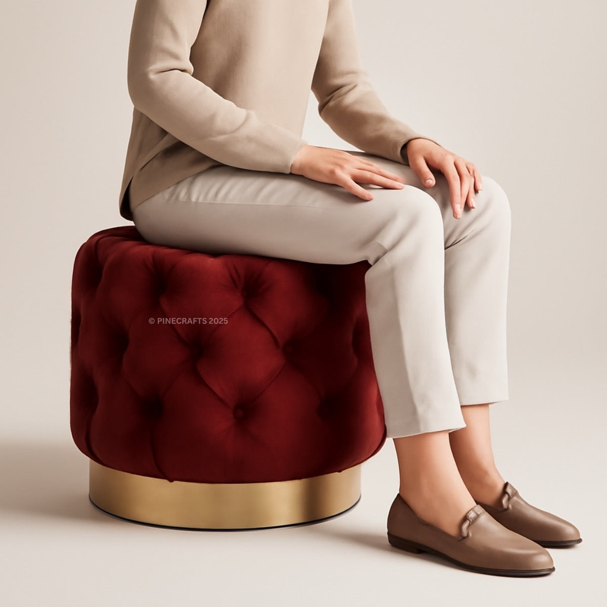 Person sitting on a red tufted stool with a gold base against a beige background