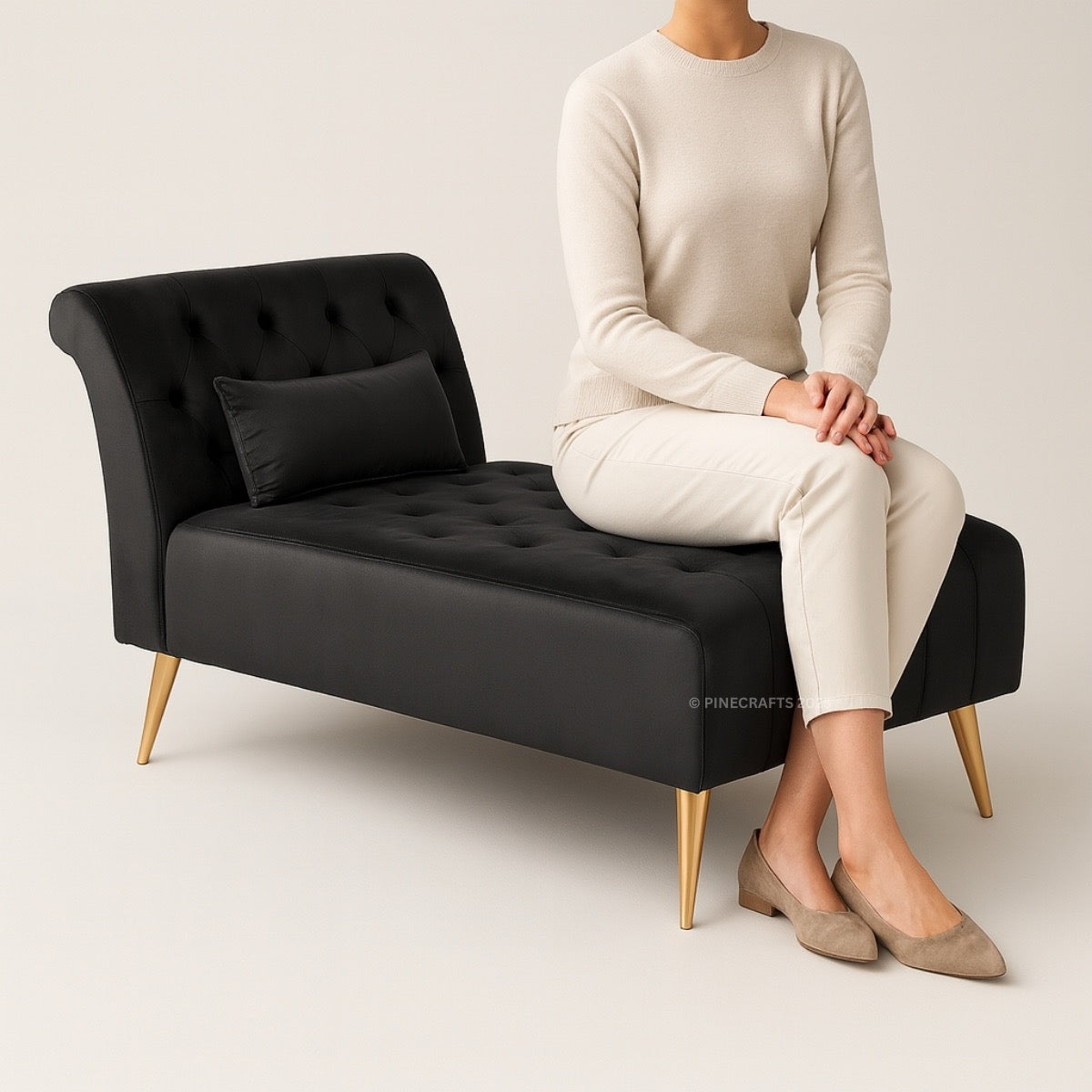Person sitting on a black tufted bench with gold legs against a plain background