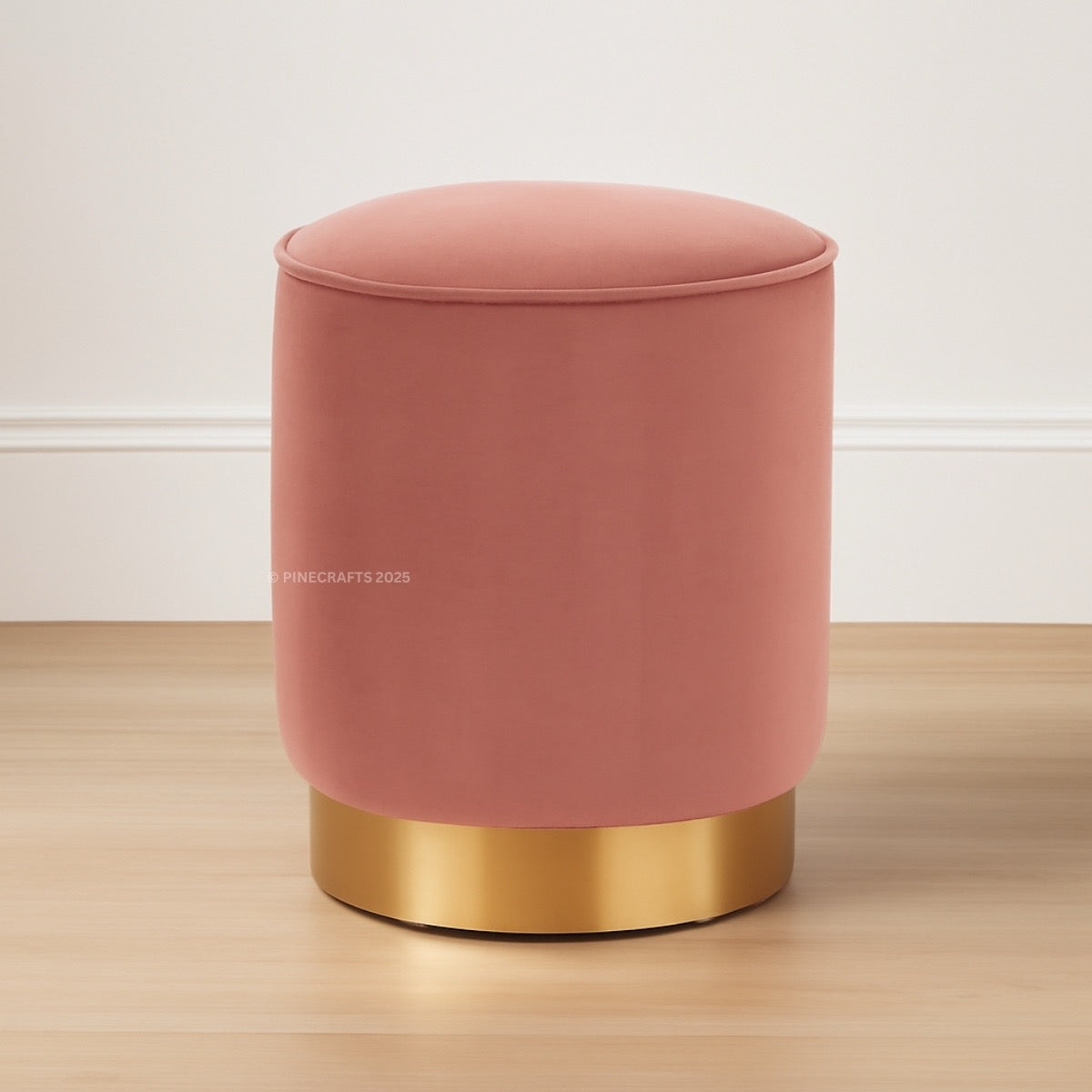 Pink velvet stool with gold base on a wooden floor