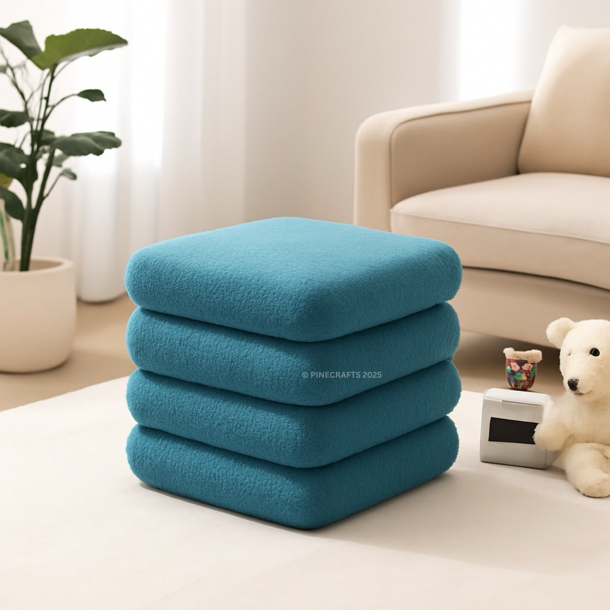 Stack of blue cushions on a white surface with a beige sofa and plant in the background