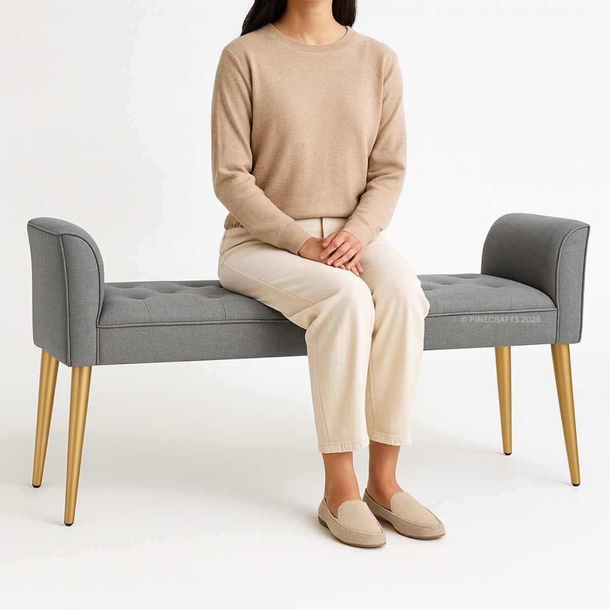 Person sitting on a gray bench with gold legs wearing a beige sweater and pants.