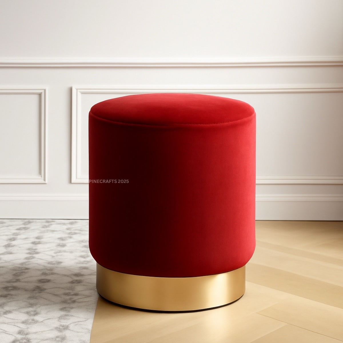 Red stool with gold base on a wooden floor against a white wall.