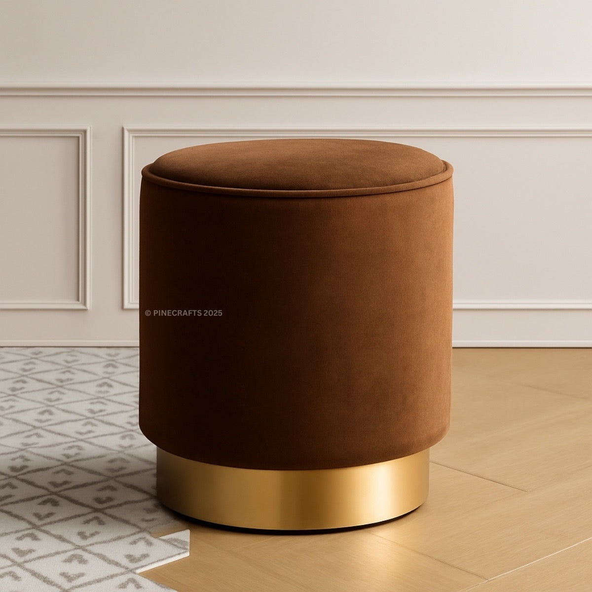 Brown velvet ottoman with gold base on a wooden floor.