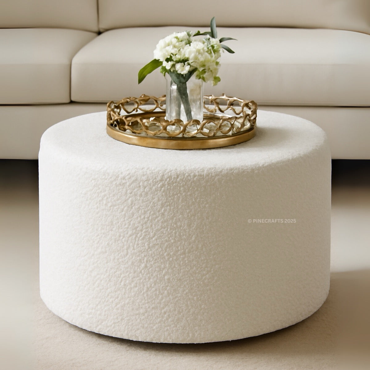 Round white ottoman with a gold tray and white flowers on a beige sofa background