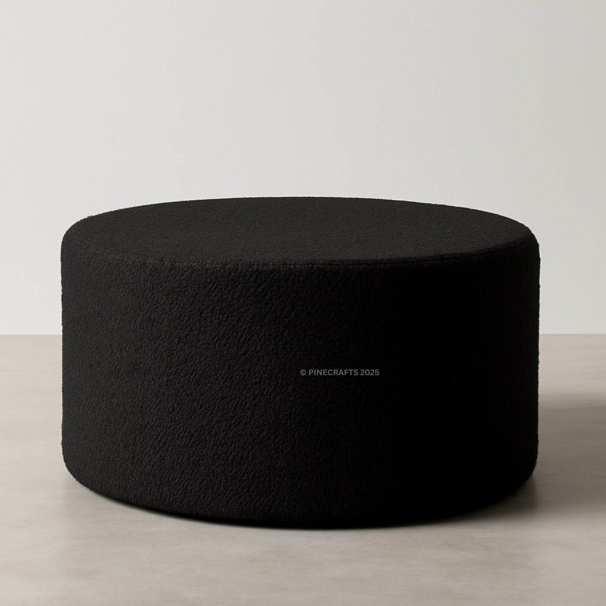 Black cylindrical ottoman on a light wooden floor with a neutral background