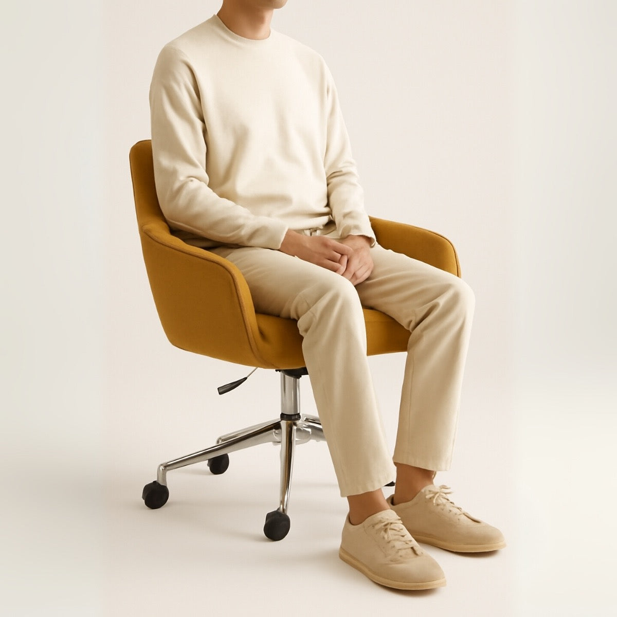 Person sitting on a mustard yellow chair wearing a cream sweater, beige pants, and shoes against a white background