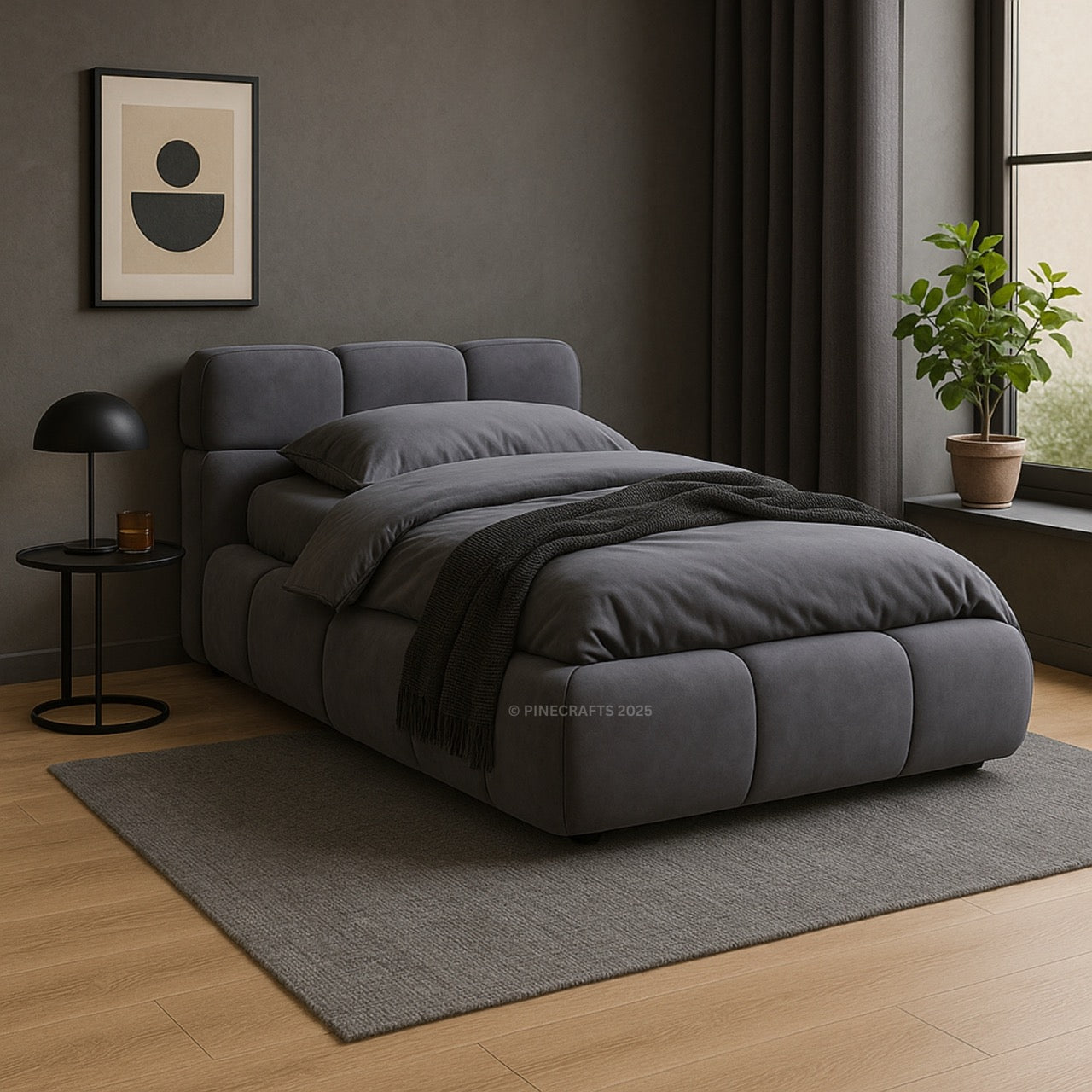 Gray upholstered bed in a room with a lamp, plant, and framed picture on the wall.